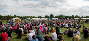 Campteilnehmer*innen / Aktivisti sitzen auf einer Campwiese, im Hintergrund große weiße Zelte
